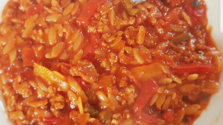 Ein gef&uuml;llter Teller mit Kritharaki-Nudeln, bedeckt von einer herzhaften Tomatensauce und buntem Gem&uuml;se, appetitlich angerichtet.