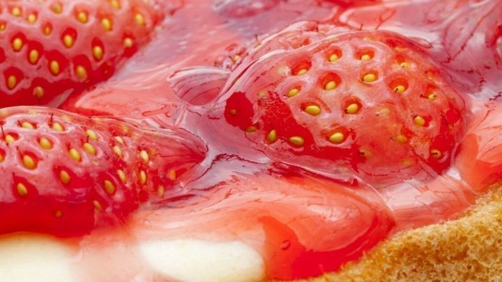 Ein fruchtiger Tortenguss mit frischen Erdbeeren bedeckt eine cremige Kuchenbasis in einem hellbraunen Keksboden.
