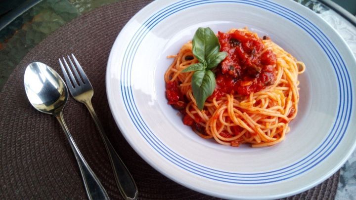 Eine Portion spaghetti liegt in einer wei&szlig;en Sch&uuml;ssel, &uuml;berzogen mit w&uuml;rzigem Tomatensugo und frischem Basilikum.
