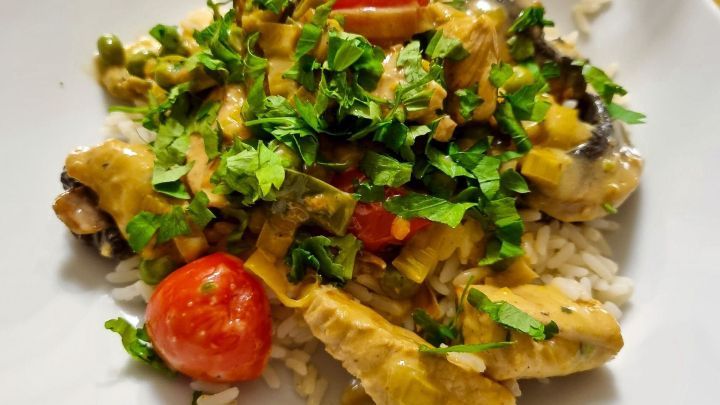 Eine bunte Reispfanne mit H&auml;hnchen, Gem&uuml;se und frischen Kr&auml;utern, serviert auf einem wei&szlig;en Teller.