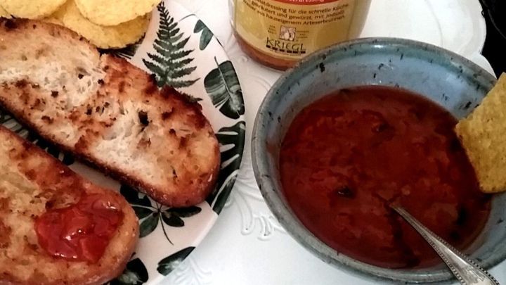 Eine sch&auml;lchen mit k&ouml;stlicher Nudelso&szlig;e als Dip steht neben ger&ouml;stetem Brot und Tortillachips auf einem Teller.