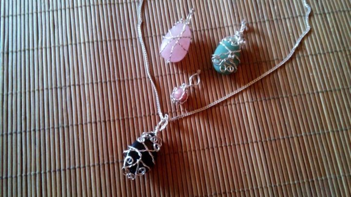 Silberdraht-Kettenanh&auml;nger h&auml;ngt an einer Schnur, umgeben von bunten, in Draht gefassten Steinen auf einem matten Untergrund.