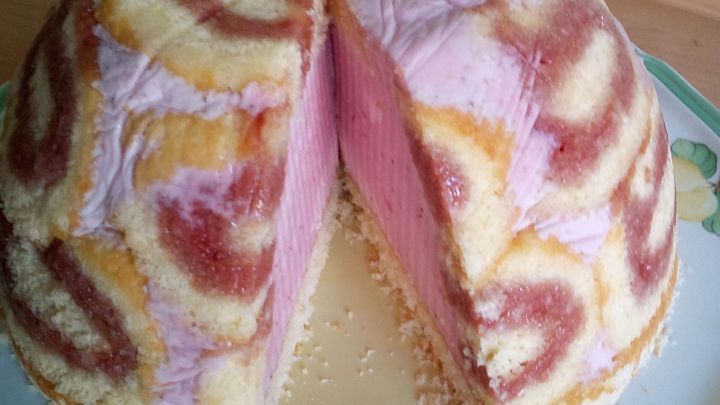Eine bunte Erdbeer-Buttermilch-Torte mit einer dekorativen Musterung, die halb auf einem Teller geschnitten ist.