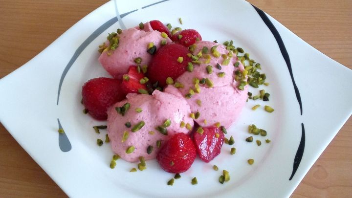 Auf einem wei&szlig;en Teller liegt eine Erdbeer-Mousse mit frischen Erdbeeren und gehackten Pistazien, sch&ouml;n angerichtet.
