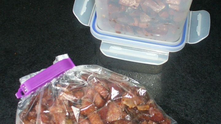 Kleine St&uuml;cke von Speck in Beh&auml;ltern, die zum Einfrieren vorbereitet sind, auf einer dunklen Oberfl&auml;che.