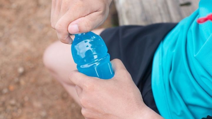 Eine Hand h&auml;lt eine Wasserflasche, w&auml;hrend sie den Verschluss &ouml;ffnet, um das Getr&auml;nk herauszuholen.