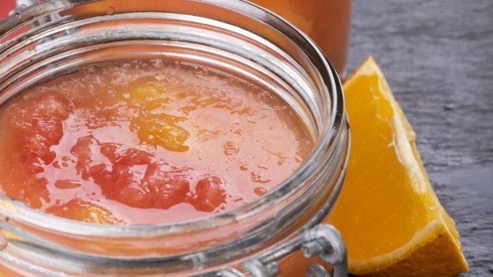 Ein Glas und ein Einmachglas mit fruchtigem Saft stehen auf einem dunklen Untergrund neben frisch geschnittenen Orangen.