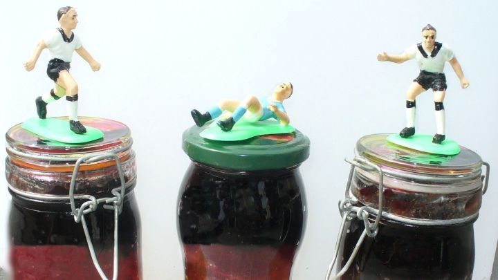 Drei Gl&auml;ser mit mehrfarbiger Deutschlandmarmelade, dekoriert mit Fu&szlig;ballfiguren, stehen auf einem Tisch.
