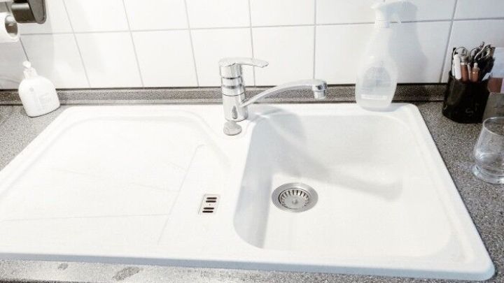 Eine wei&szlig;e Granitsp&uuml;le steht auf einer Arbeitsplatte, w&auml;hrend ein Wasserhahn &uuml;ber ihr schwenkt und die Wand gefliest ist.