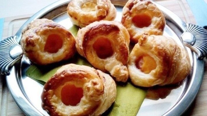 Kleine Aprikosenplunder liegen appetitlich auf einem silbernen Teller, umgeben von einer gr&uuml;nen Serviette.