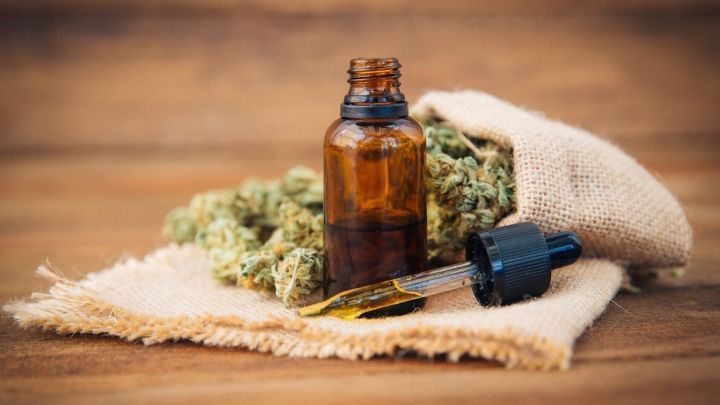 Ein braunes Fl&auml;schchen mit Tropfer steht auf einer stofflichen Unterlage, umgeben von Cannabisbl&uuml;ten, vermittelt Harmonie.