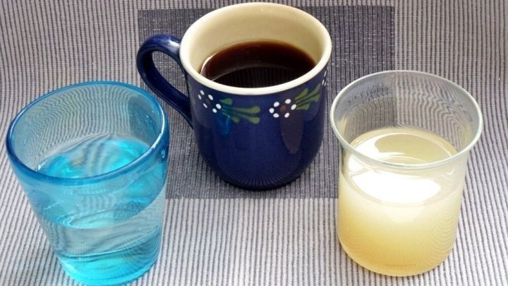 Drei Gl&auml;ser stehen auf einem Tisch: ein blaues Glas mit Wasser, eine Tasse Kaffee und ein wei&szlig;er Saft.