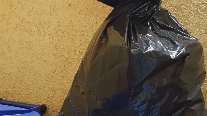 Schwarze M&uuml;llt&uuml;te steht auf einem Container, um die Abf&auml;lle von Tieren fernzuhalten, in einem urbanen Umfeld.