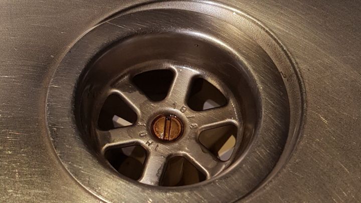 Ein Abfluss aus Edelstahl ist sichtbar, w&auml;hrend ein Geschirrsp&uuml;ltab verwendet wird, um ihn zu reinigen.