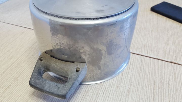 Ein damit bearbeiteter Topf liegt auf einem Tisch, dessen Griff besch&auml;digt ist, was auf unsachgem&auml;&szlig;e Reinigung hinweist.