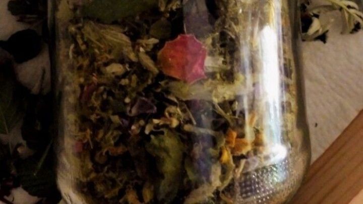 Ein Glas gef&uuml;llt mit getrockneten Bl&uuml;ten und Bl&auml;ttern, zur Herstellung einer Bl&uuml;tenteemischung, steht auf einem Holztisch.