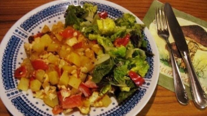 Eine bunte Kartoffel-Eier-Pfanne liegt auf einem Teller, w&auml;hrend ein frischer Salat daneben serviert wird.