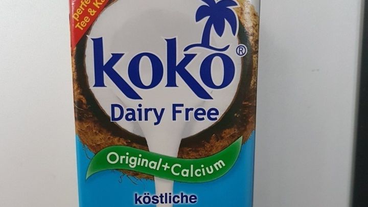 Ein Karton mit "koko Dairy Free" Pflanzenmilch steht auf einer Arbeitsfl&auml;che und zeigt den Inhalt, der gerade ausgegossen wird.