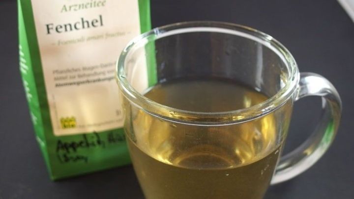 Ein Glas Fencheltee steht vor einer gr&uuml;nen Verpackung mit der Aufschrift "Fenchel", umgeben von einem dunklen Hintergrund.