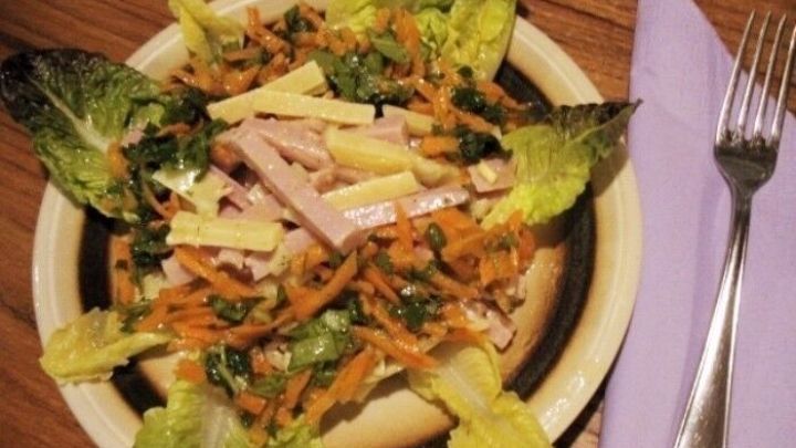 Frischer K&auml;se-Schinken-Salat mit Rucola liegt auf einem Teller, umgeben von knackigem Salat und einer Gabel.