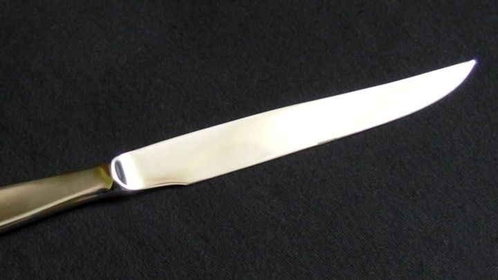 Ein gl&auml;nzendes Edelstahlmesser liegt auf schwarzem Stoff, bereit zum Schneiden in einer eleganten K&uuml;chenumgebung.