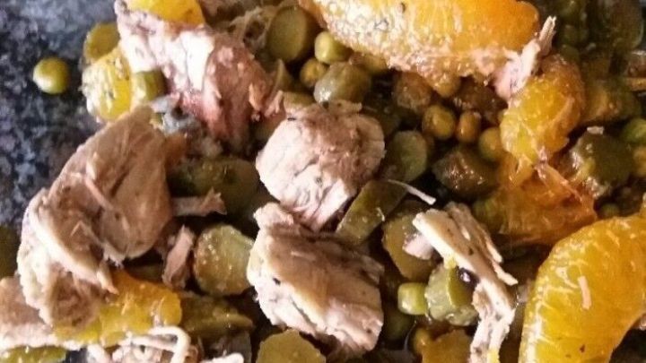 Ein bunter Sommer-H&auml;hnchen-Salat liegt auf einem gl&auml;sernen Teller, kombiniert mit Erbsen und Mandarinenst&uuml;cken.