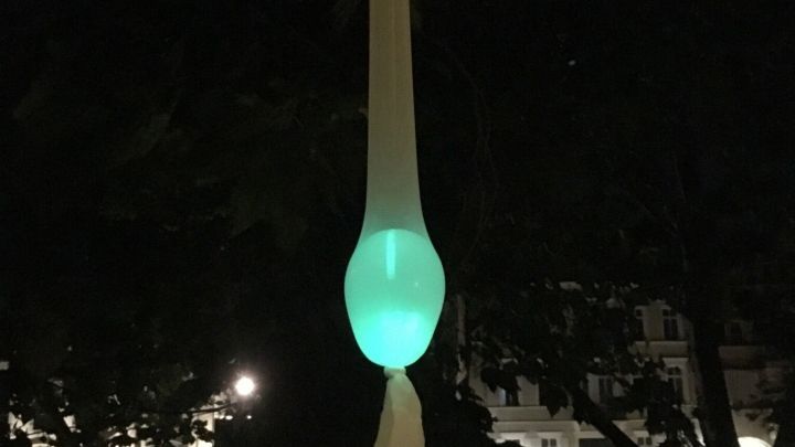 Ein leuchtender Lichtballon h&auml;ngt in einem dunklen Park, w&auml;hrend er sanft in der Nacht strahlt.