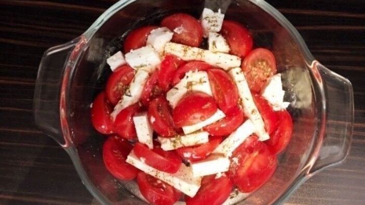 Saftige Tomaten sind in einer Glasform angeordnet und mit Feta und Kr&auml;utern garniert, bereit zum Backen als Gratin.