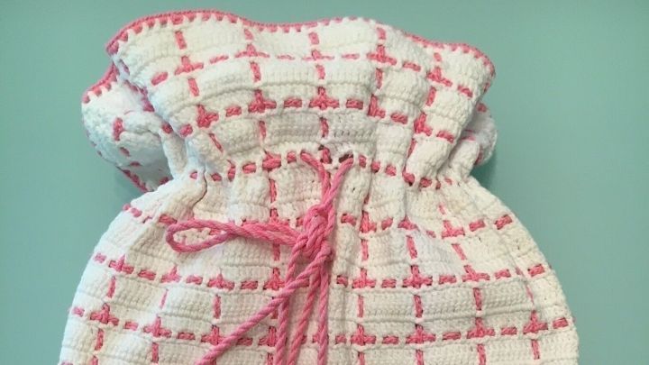 Eine W&auml;rmflasche, die als Kaltflasche umfunktioniert wurde, liegt auf einem blauen Untergrund; sie zeigt ein kariertes Muster mit pinken Akzenten.