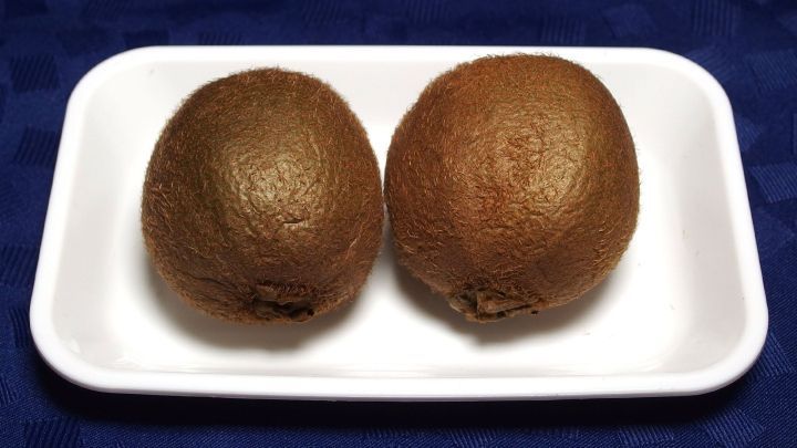 Zwei Kiwi liegen auf einem wei&szlig;en Teller, bereit zum Verzehr, in einem hellblauen Umfeld, das einen gesunden Snack symbolisiert.