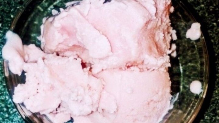 Eine gl&auml;serne Sch&uuml;ssel enth&auml;lt cremiges, rosafarbenes Eis ohne Eismaschine, serviert auf einer dunklen Tischoberfl&auml;che.