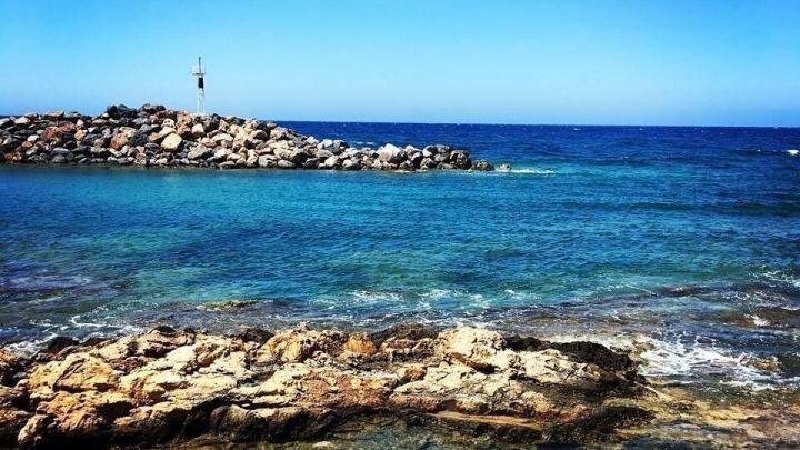 Kristallklares Wasser umsp&uuml;lt gro&szlig;e Steine, w&auml;hrend der Blick &uuml;ber das Meer unter einem strahlend blauen Himmel schweift.