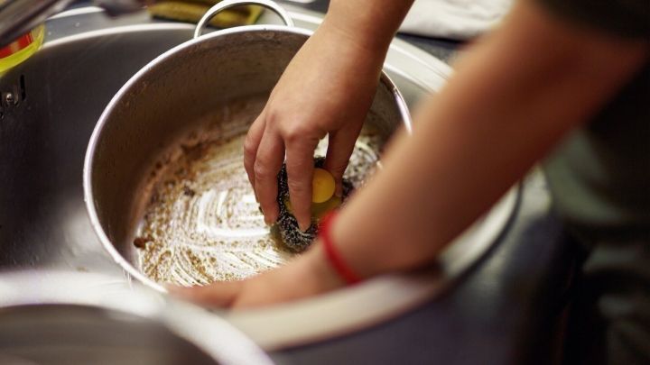 Ein Arm greift in einen angebrannten Kochtopf und entfernt mit einer Handfl&auml;che den Kaffeesatz im Waschbecken.