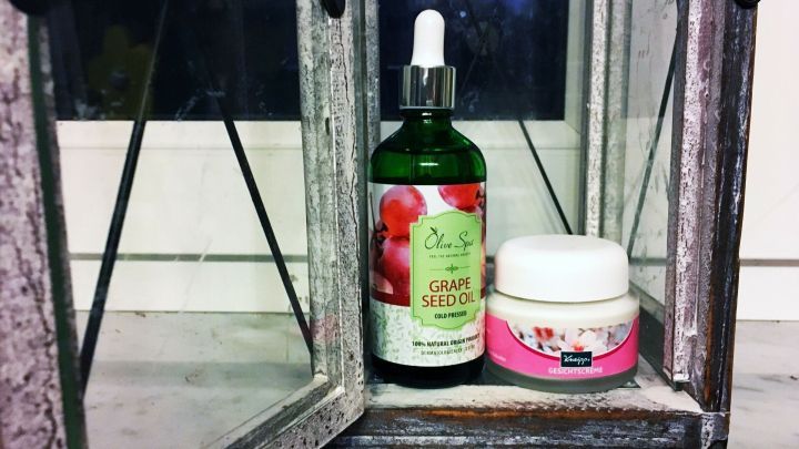 Eine Flasche Traubenkern&ouml;l und eine Augencreme stehen in einem dekorativen Regal. Sie sind umgeben von einem rustikalen, transparenten Beh&auml;lter.