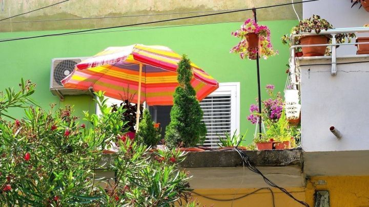 Ein Sonnenschirm steht auf einem Balkon, w&auml;hrend Pflanzen im Hintergrund mit einer bunten Wand harmonieren.