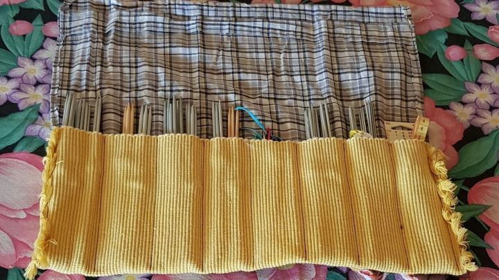 Ein gen&auml;htes Stoffetui f&uuml;r Nadelspiele liegt ausgebreitet auf einem floralen Hintergrund und zeigt mehrere F&auml;cher.