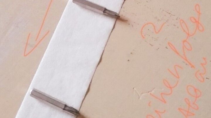 Eine Leiste mit Schraubenzubeh&ouml;r ist auf einem Tisch befestigt, w&auml;hrend Notizen und Pfeile eine Anleitung zum M&ouml;belaufbau geben.