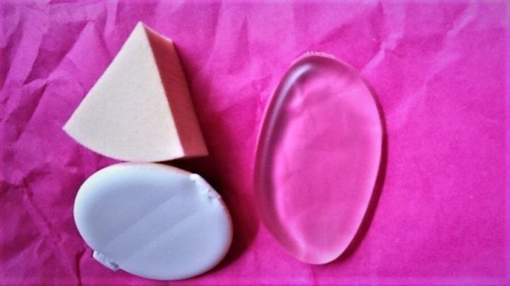 Drei Make-up-Tools: ein Silikonpad, ein ovaler Sponge und ein dreieckiger Schwamm liegen auf pinkem Papier.