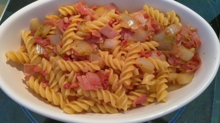 Schinken-Nudeln mit Chicoree liegen appetitlich in einer Sch&uuml;ssel, gemischt mit Zwiebeln, auf einem Tisch in einer modernen K&uuml;che.