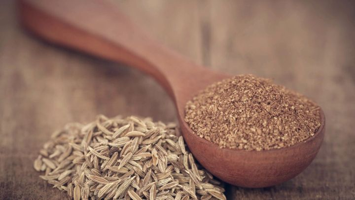 Ein Holzl&ouml;ffel mit gemahlenem K&uuml;mmel und ganzen K&uuml;mmelsamen auf einer rustikalen Holzoberfl&auml;che, die zur Linderung von Sodbrennen dienen k&ouml;nnen.