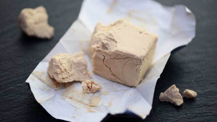 Ein St&uuml;ck Hefe liegt auf einem wei&szlig;en Papier, umgeben von zerbr&ouml;ckelten Hefest&uuml;cken, bereit zur Verwendung in der Obstfliegenfalle.