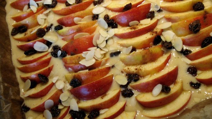 Der frisch gebackene Apfelkuchen ist mit abgeschnittenen &Auml;pfeln, Mandeln und Rosinen belegt und auf einem Backblech angerichtet.