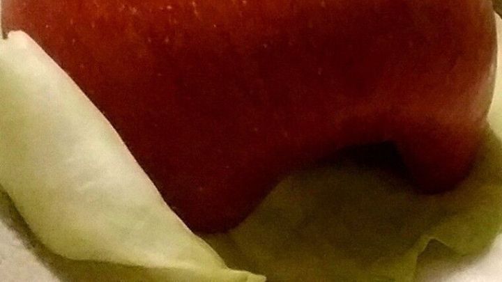 Ein roter Apfel liegt auf frischen Kohlbl&auml;ttern in einer gesch&uuml;tzten Umgebung, bereit zum Verzehr oder zur Pr&auml;sentation.