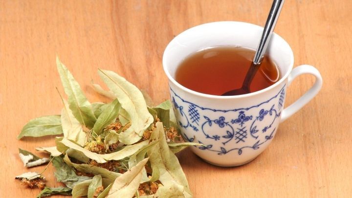 Eine Tasse Tee steht auf einem Holzuntergrund, begleitet von getrockneten Kr&auml;utern, die rheumatische Beschwerden lindern k&ouml;nnten.