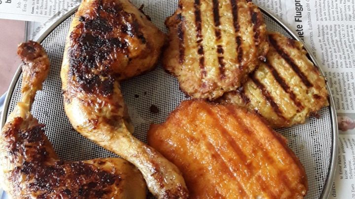 Auf einem Teller liegen gebratene H&auml;hnchenschenkel neben ger&ouml;steten Beilagen, die auf Zeitungspapier abtropfen.