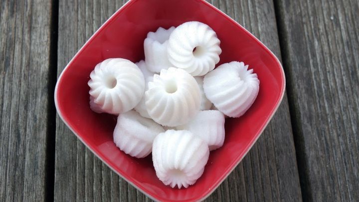 Ein rotes Sch&auml;lchen enth&auml;lt mehrere kleine, wei&szlig;e Zucker-Gugelhupfformen, die auf einem dunklen Holzuntergrund arrangiert sind.