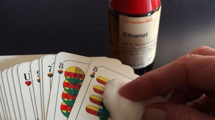Auf einem Tisch liegt ein Stapel Spielkarten, w&auml;hrend eine Hand mit einem Wattebausch Ethanol verwendet, um die Karten zu reinigen.