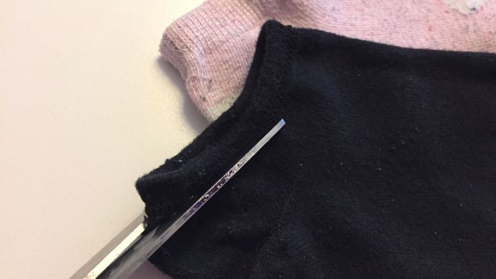 Eine alte Socke wird mit einer Schere geschnitten, um einen Haargummi herzustellen. Der Hintergrund ist schlicht und neutral.