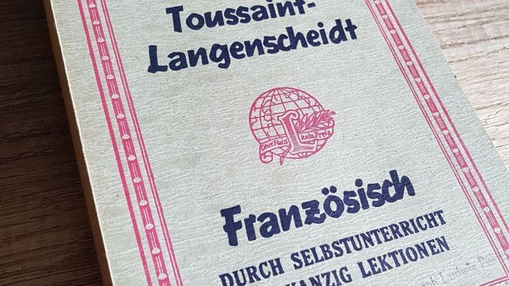 Eine alte Buchh&uuml;lle liegt auf einem Holzuntergrund. Es handelt sich um ein Franz&ouml;sisch-Lernbuch, das Gebrauchsspuren zeigt.