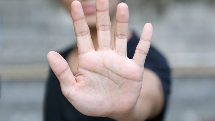 Eine ausgestreckte Hand zeigt ein deutliches "Nein". Der Hintergrund ist unscharf und wirkt urban.